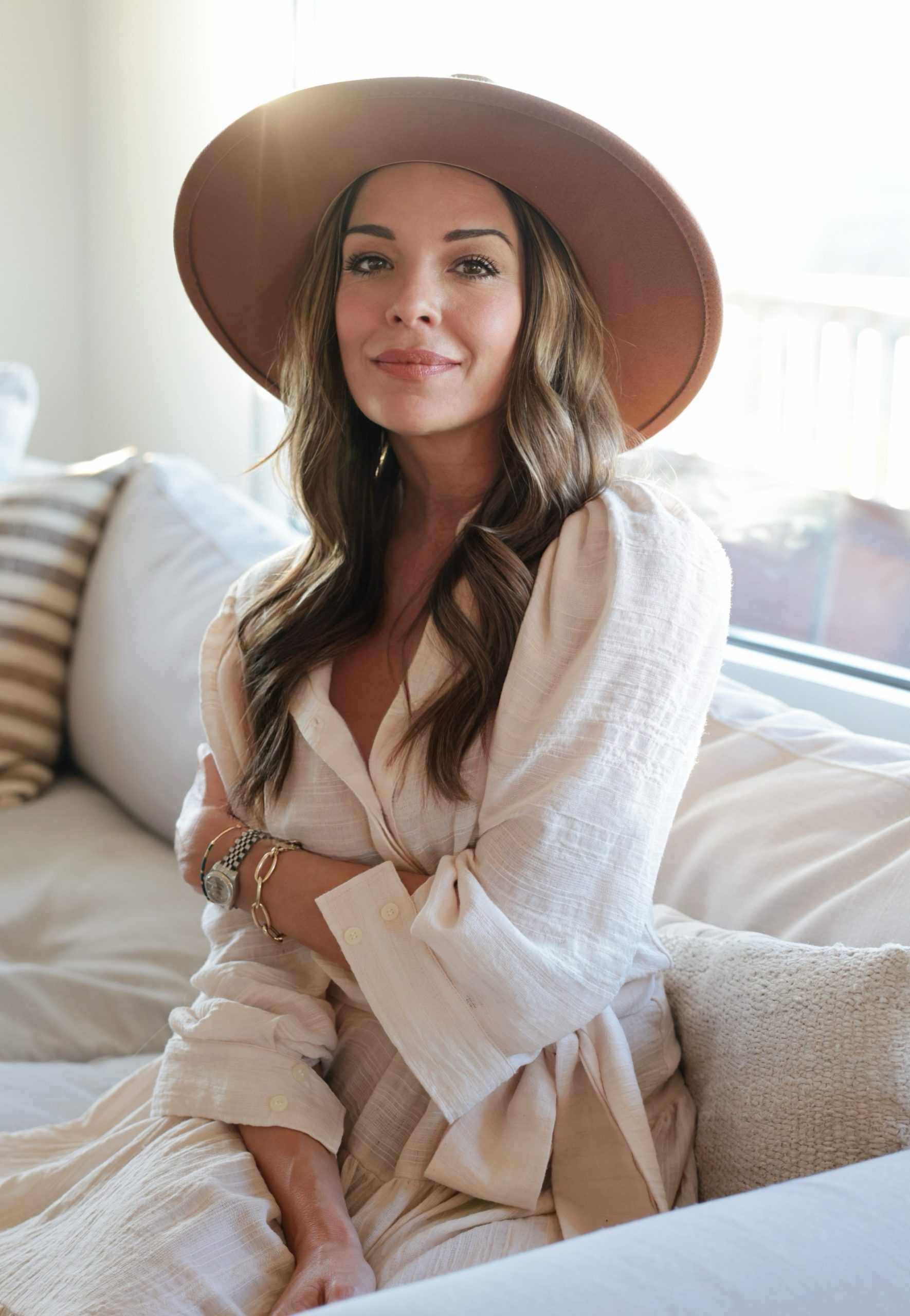 Woman wearing a wide-brim hat and white outfit, sitting on a sofa in natural light – featured guest at the Home Design and Remodeling Show.