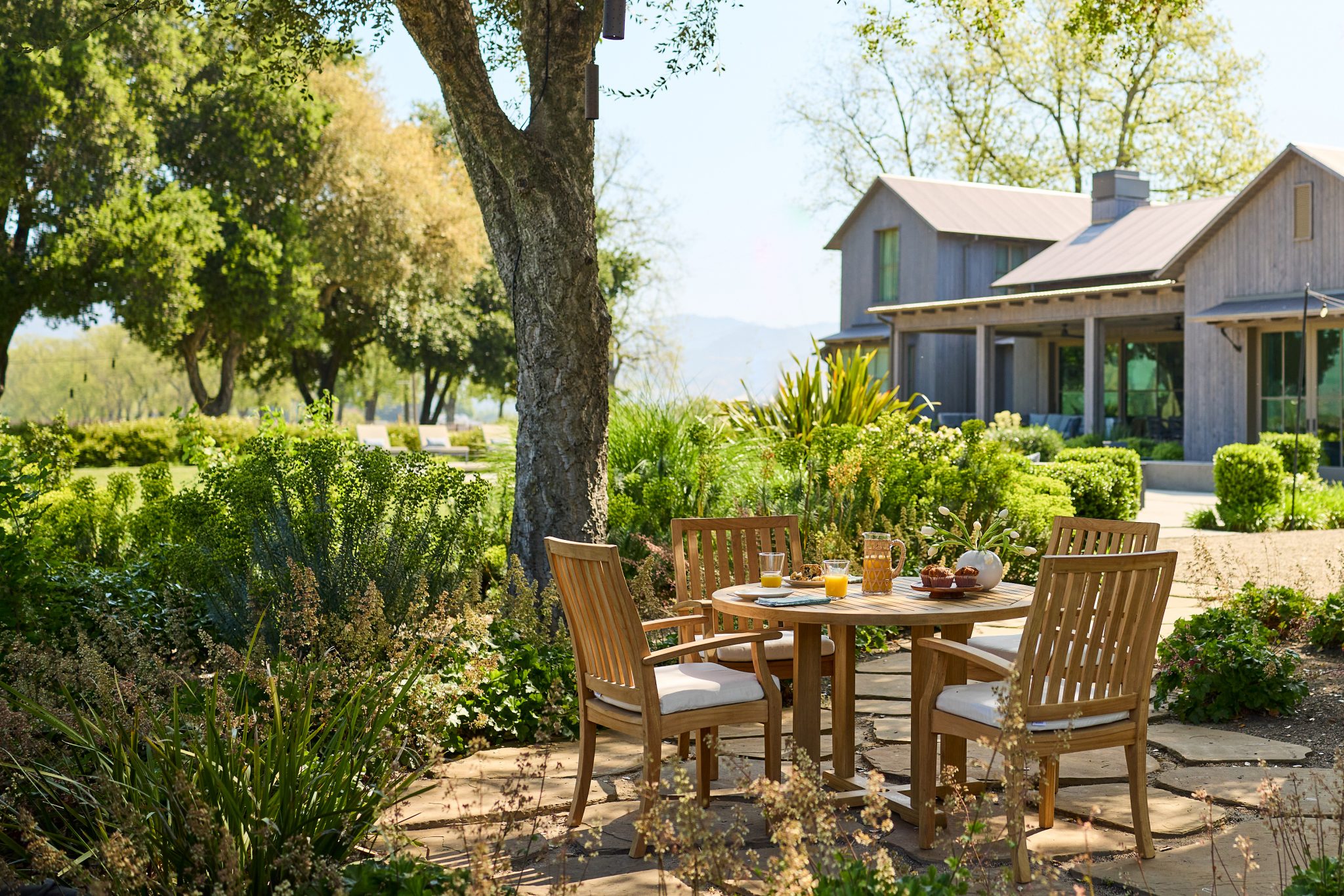 Outdoor dining area with wooden furniture and trees displayed at the Home Design and Remodeling Show.