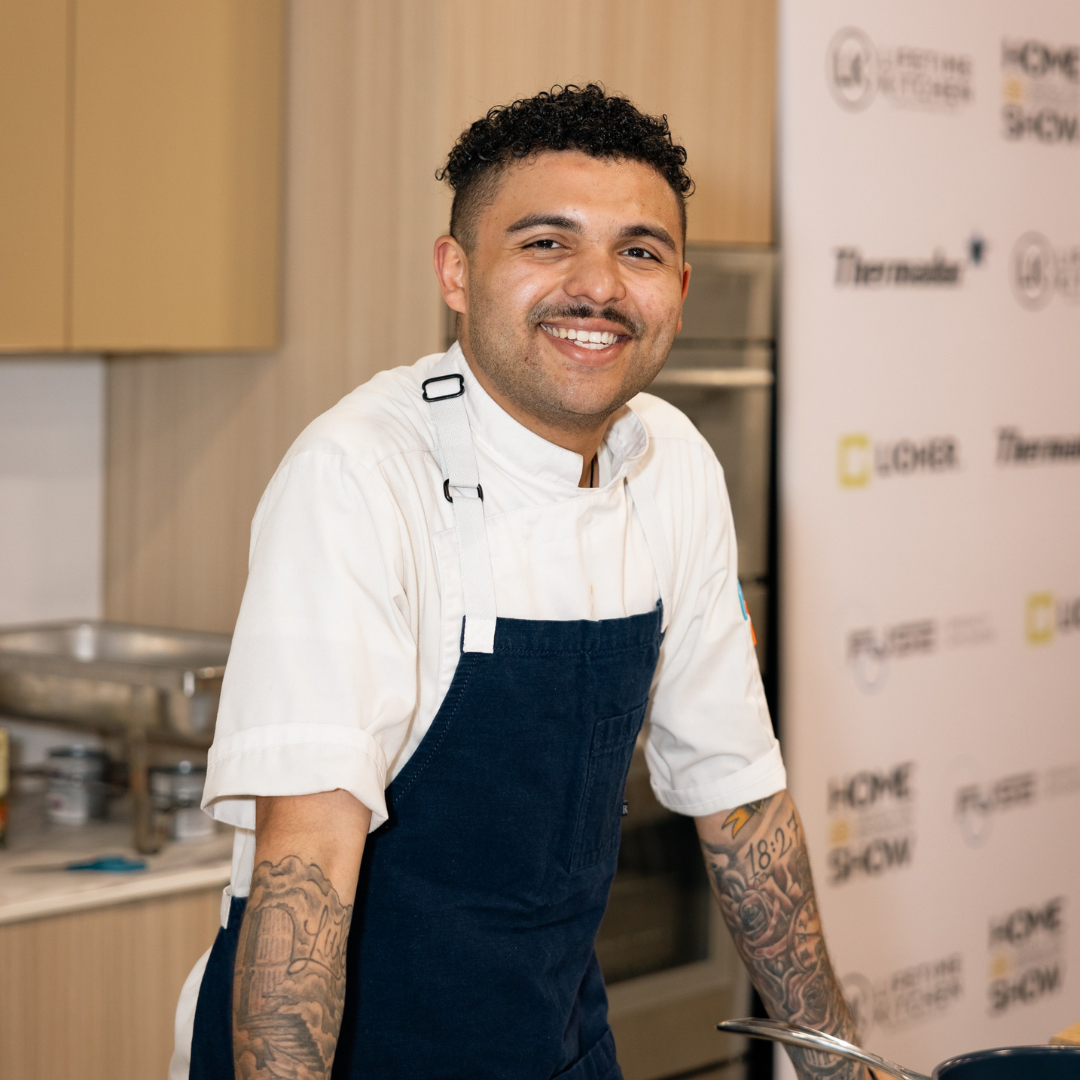 Chef smiling in a kitchen during a live cooking demonstration at the Home Design and Remodeling Show.